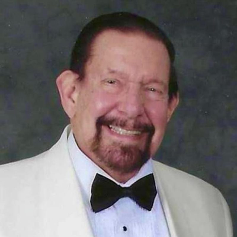 Man smiling at the camera wearing white suit and black bowtie