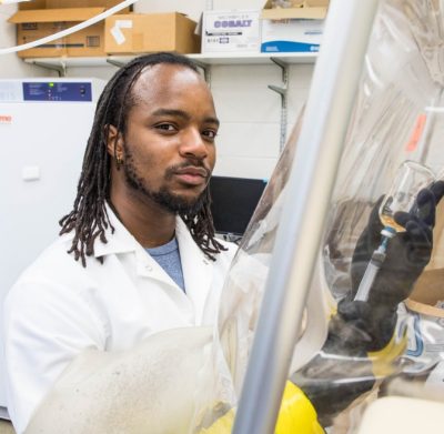 A Virginia Tech biochemistry undergraduate student uses a syringe to retrieve solution in a glass bottle in an anaerobic glove chamber.