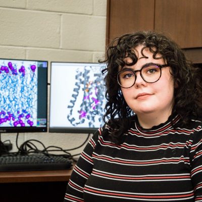A Virginia Tech biochemistry graduate students sits in front of a computer with protein simulations displayed.