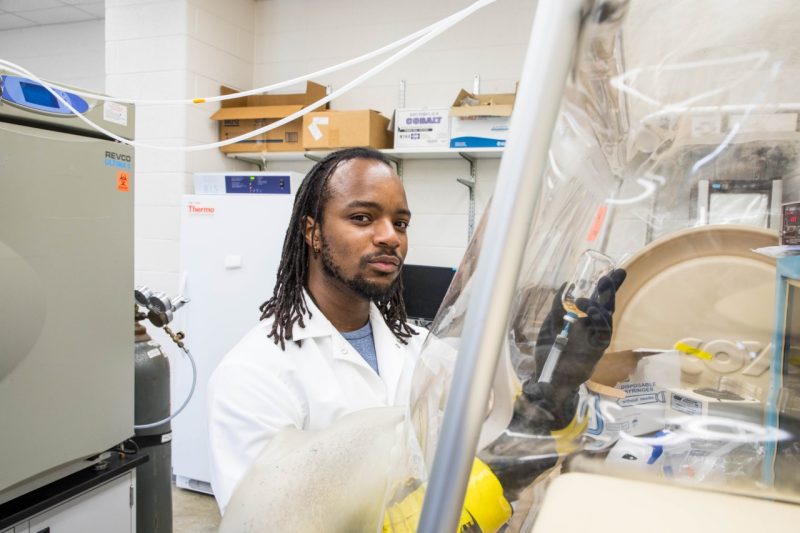 A Virginia Tech biochemistry undergraduate student uses a syringe to retrieve solution in a glass bottle in an anaerobic glove chamber.