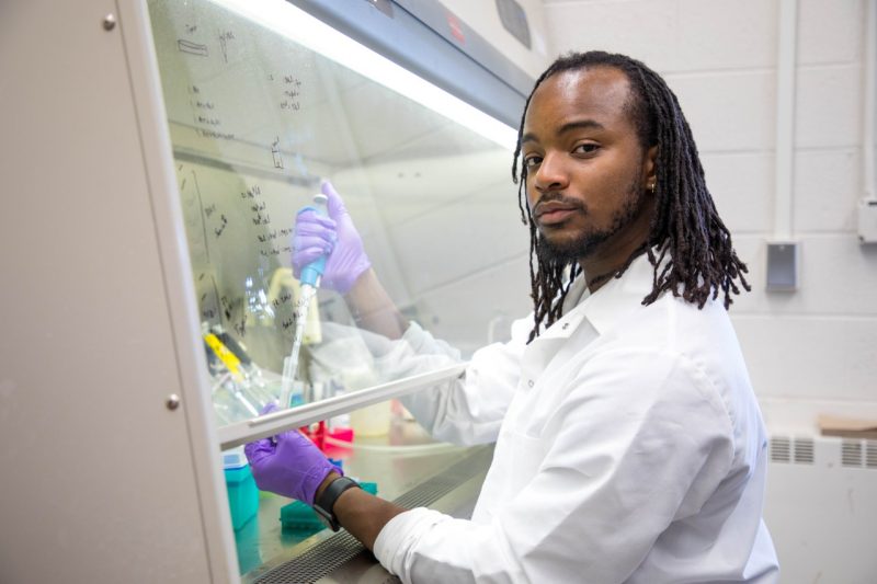 Student holding a pipette under a fume hood in lab