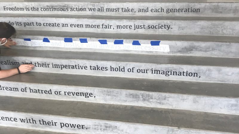  A masked Moss Arts Center graduate assistant helps to install a quote from John Lewis on the risers of the steps from the Grand Lobby to the Francis T. Eck Exhibition Corridor