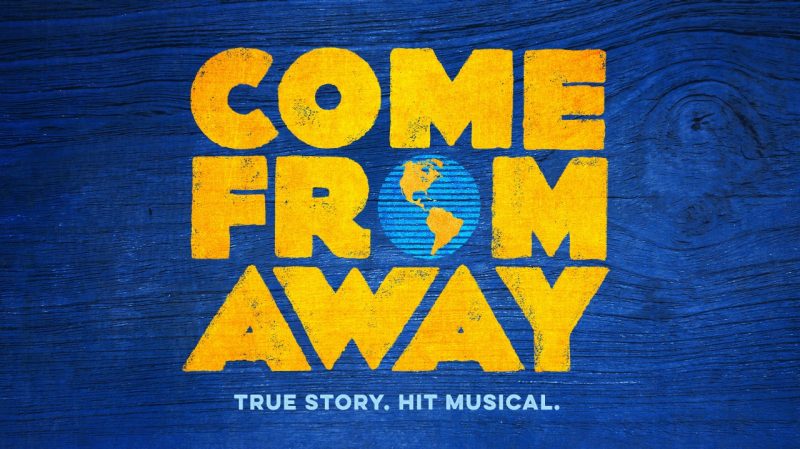  The logo for Broadway show "Come From Away," which is spelled out in yellow text with the O in "From" represented as the earth. Below the title is light blue text that reads "True Story. Hit Musical." The background is a blue woodgrain.