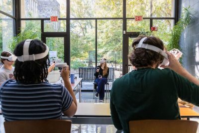 Three students seated inside wearing virtual reality headsets and controllers.
