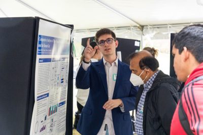 A faculty member and student look at a poster while the student presenter points and looks towards the sky.