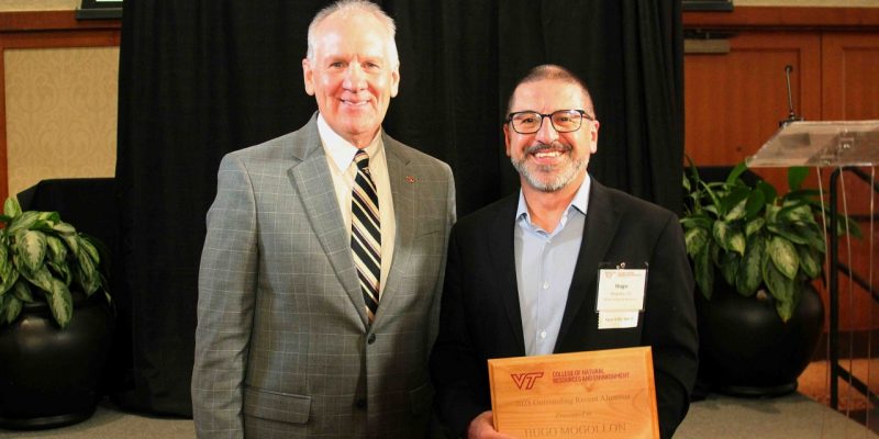 Paul Winistorfer stands next to Hugo Mogollon holding a wooden award plaque