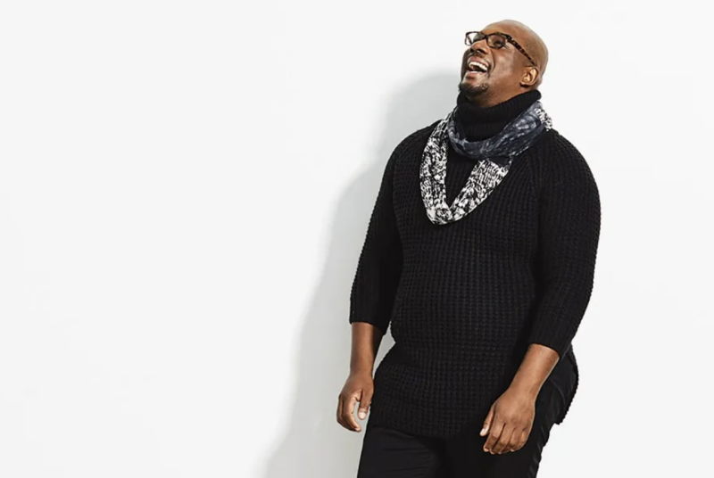 Harold Steward, wearing black top and pants, black and white scarf, laughing