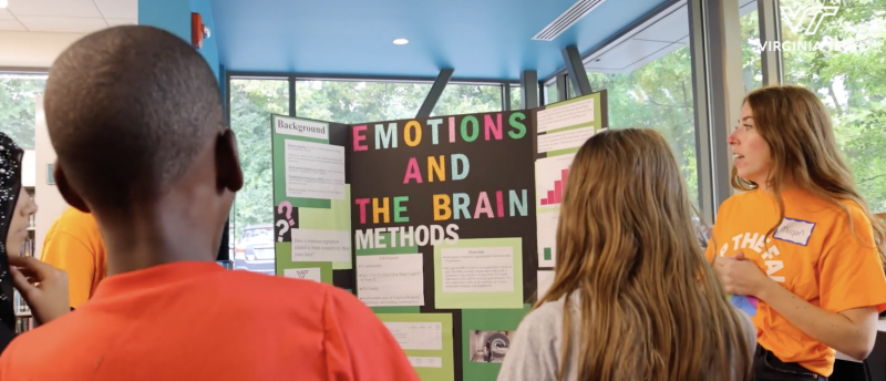 Grad. Student with children around a science poster