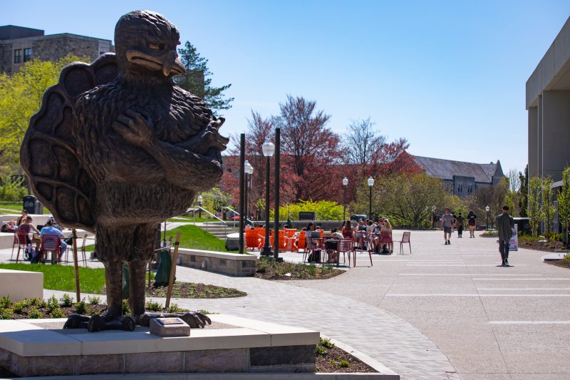 Big bronze HokieBird on the Quillen Spirit Plaza in front of Dietrick Hall with students in outdoor seating